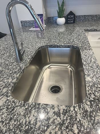 A kitchen sink with a granite countertop and a silver faucet.